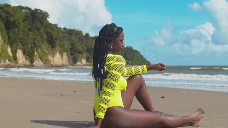 African-girl-in-a-bikini-sits-in-the-sand-with-ocean-waves-crashing-in-the-background