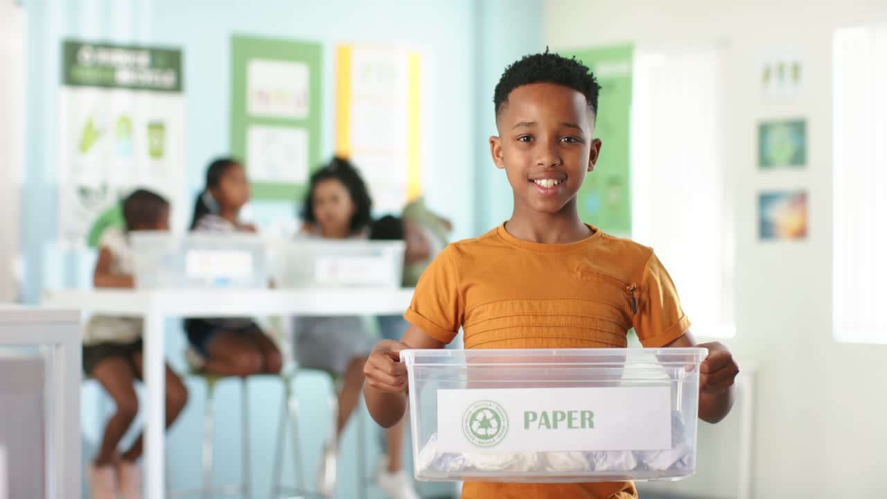 African American children sorting in recycling lesson with boy in orange holding bin labeled PAPER