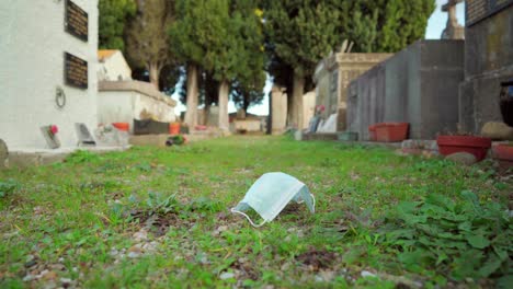 death by covid-19 pandemic, protective face mask discarded on the ground in a cemetery or graveyard, graves and tombs in the background