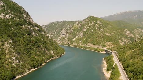 rising aerial view over a wide part of the neretva river with a bridge over a tributary in bosnia with the road at the foot of the mountains