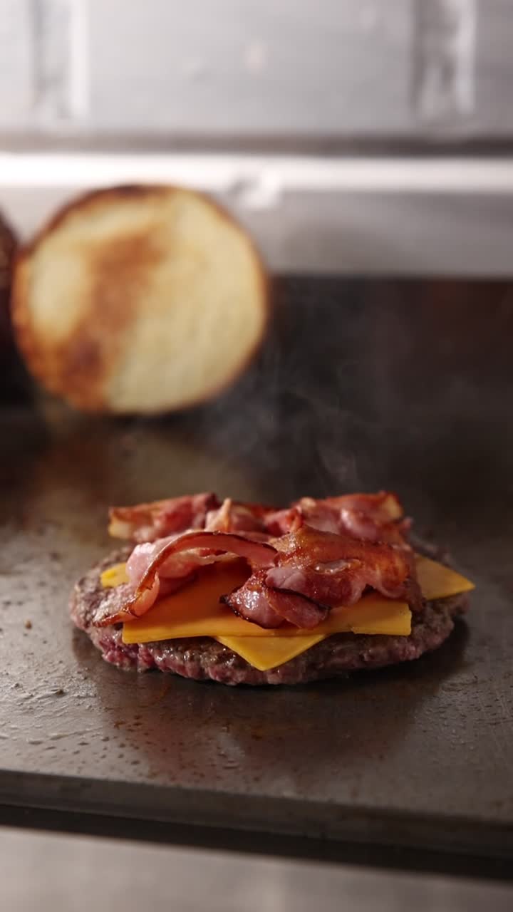 Lo chef ricopre un hamburger con formaggio e bacon sulla piastra