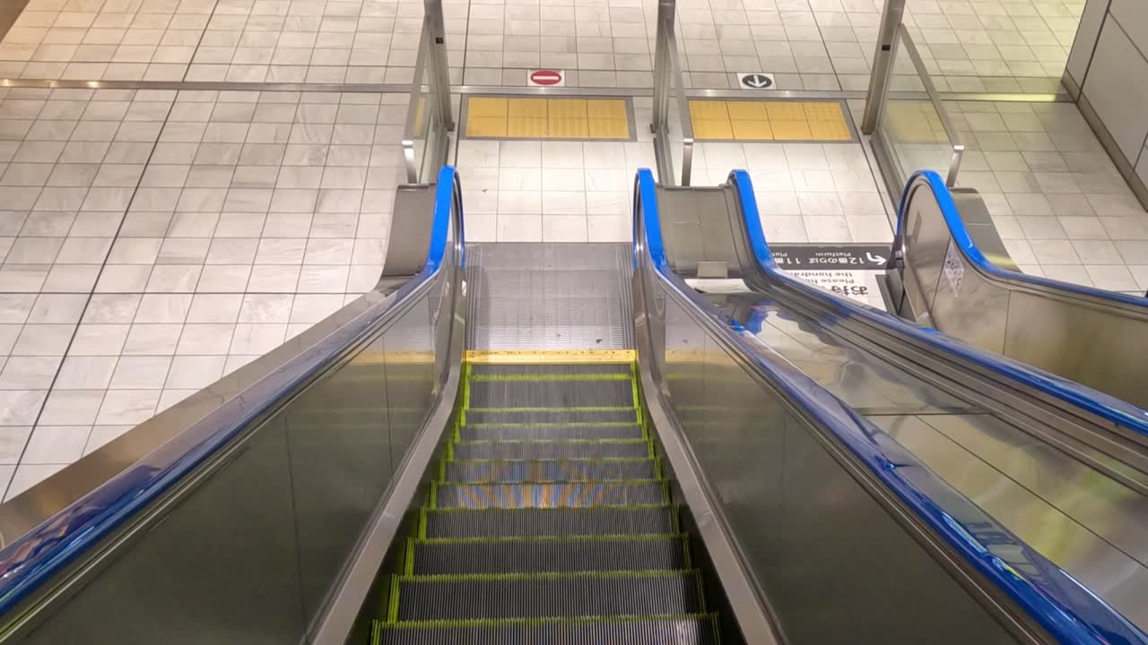 Et førstepersonsperspektiv, der bevæger sig ned ad en ren, moderne rulletrappe mod et flisebelagt stationsgulv