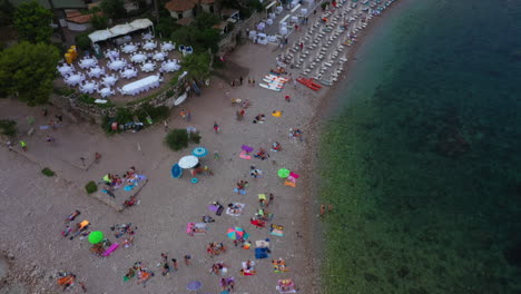 Drohne-Fliegt-über-Die-Ecke-Eines-überfüllten-Strandes-Und-Neigt-Sich-Langsam-Nach-Oben,-Um-Wunderschöne-Berge-Freizulegen