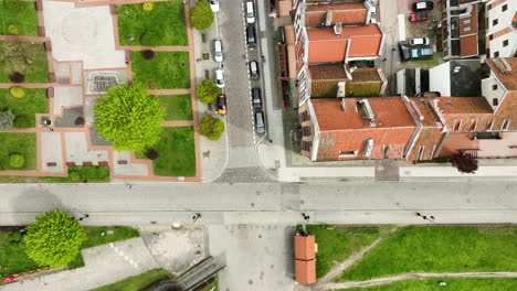 Directly-overhead-aerial-view-of-a-street-in-Elbląg,-showcasing-a-pedestrian-area-with-vibrant-green-trees,-surrounded-by-the-town's-characteristic-red-roofed-buildings