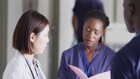 video of three diverse male and female doctors talking in hospital corridor discussing file