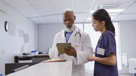 Diverse-male-and-female-doctors-using-tablet-and-talking-at-hospital