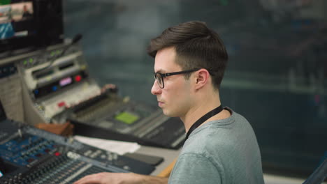 focused broadcast operator managing equipment and monitors in control room, adjusting settings on sound desk and video mixing board for live production