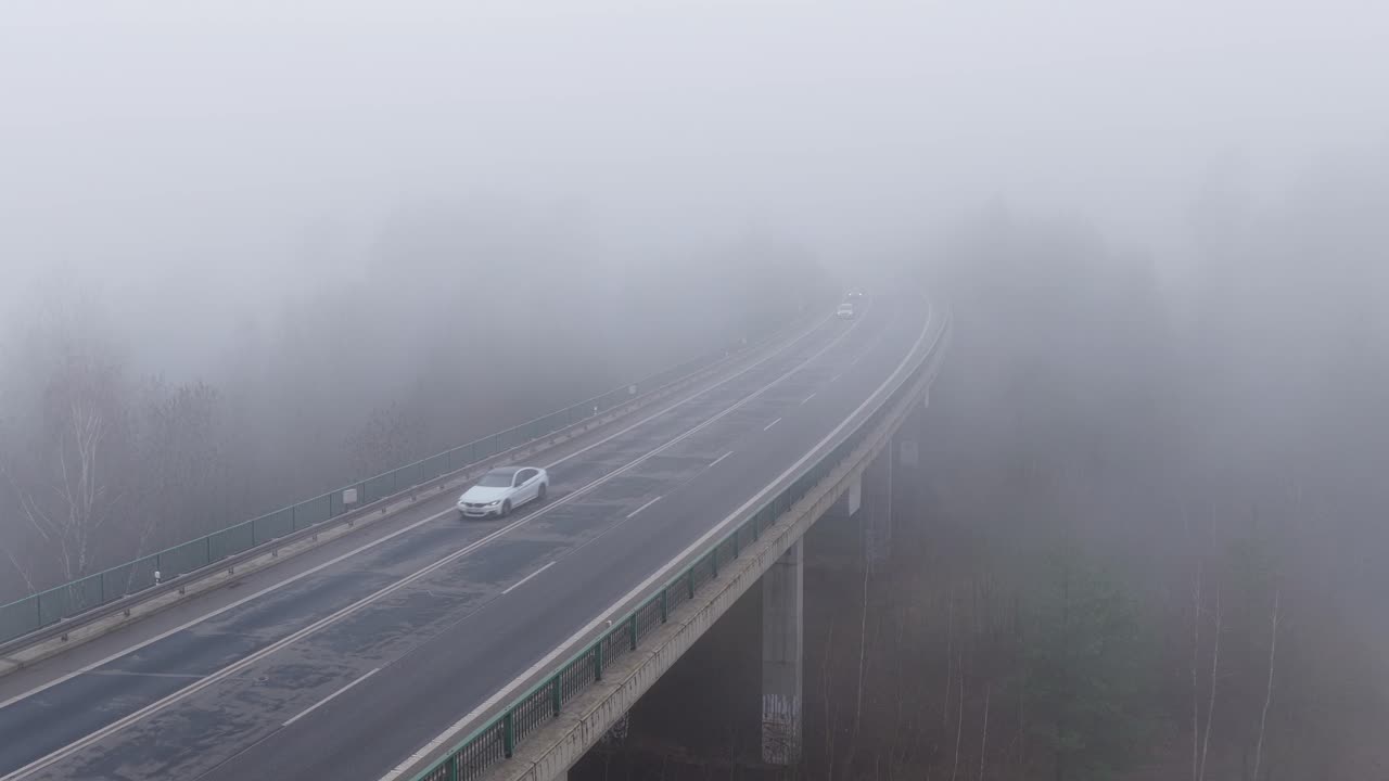 Foggy bridge scene with vehicles driving through mist on a rainy day creating a moody and eerie feeling