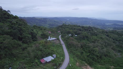 Unidades-De-Automóviles-En-Una-Pequeña-Carretera-Con-Casas-A-Un-Lado-En-La-Isla-De-Sumba-Indonesia,-Antena