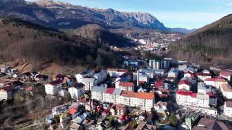 Aufsteigende-Drohnenaufnahme-Des-Dorfes-Sinaia-In-Rumänien-Bei-Sonnenlicht-Und-Blauem-Himmel-Zwischen-Hügeln