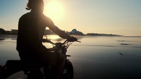 man riding motorcycle on a beach at sunrise