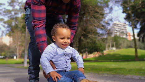 boy lying on skateboard, rolling with fathers help