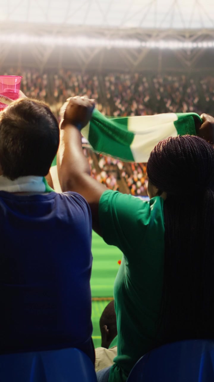 Video vertical: Vista trasera de la afición de fútbol cantando enérgicamente en el estadio, sosteniendo bebidas.