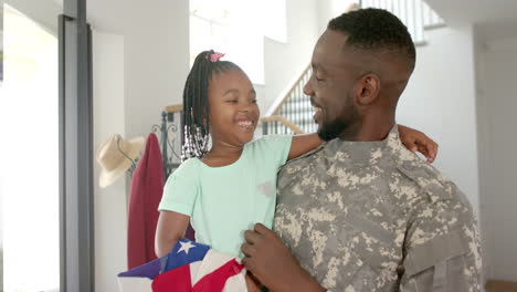 african american father in military uniform holds a young daughter with braided hair at home