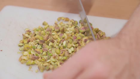 chef finely chopping green pistachios on a white cutting board in slow motion, close-up