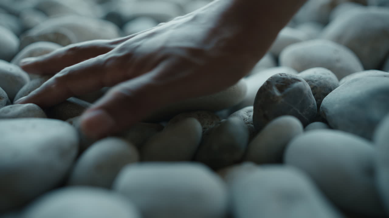 Hand touching smooth pebbles on Sicily beach macro detail