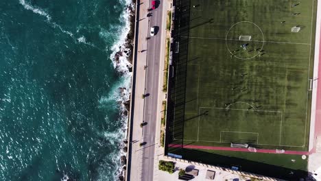 Hermoso-Mar-Azul-Y-Campo-De-Fútbol-Verde,-Vista-Aérea-De-Arriba-Hacia-Abajo