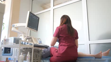 a female vascular surgeon performs an ultrasound examination of an elderly patient’s vein. treatment of varicose veins of the legs