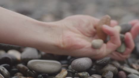 Hands-holding-and-grasping-onto-pebbles-on-stone-beach