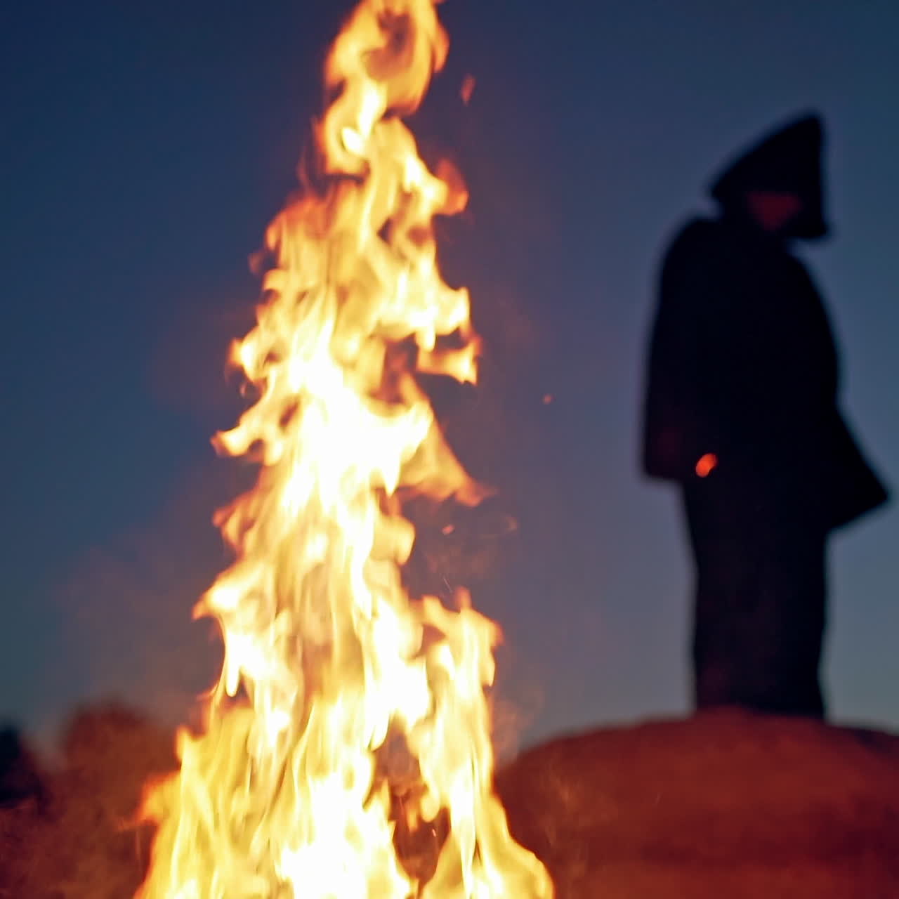 Huge flame and some smoke on the background of black figure outdoors. Silhouette of death on the hill at night. Vivid flame and spooky person.