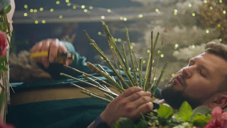 male professional florist cuts stems of fresh flowers in flower shop