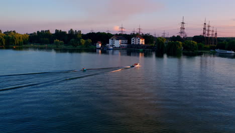 People in motor boat at sunset. Boats floating along the river on the background of power station in nature. Beautiful orange sunlight over the river. Aerial view.