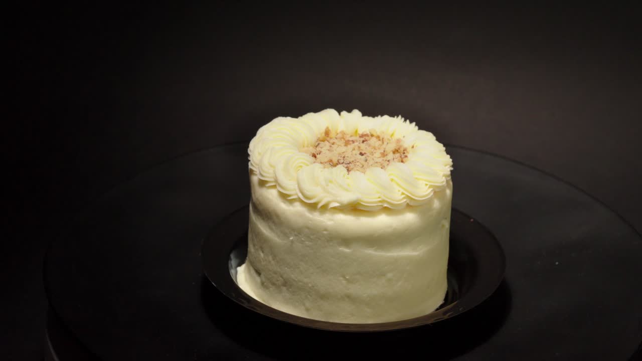 Fetta individuale di torta di carote con glassa e noci, su un piatto girevole con sfondo nero, isolata. Dolce delizioso e sano.