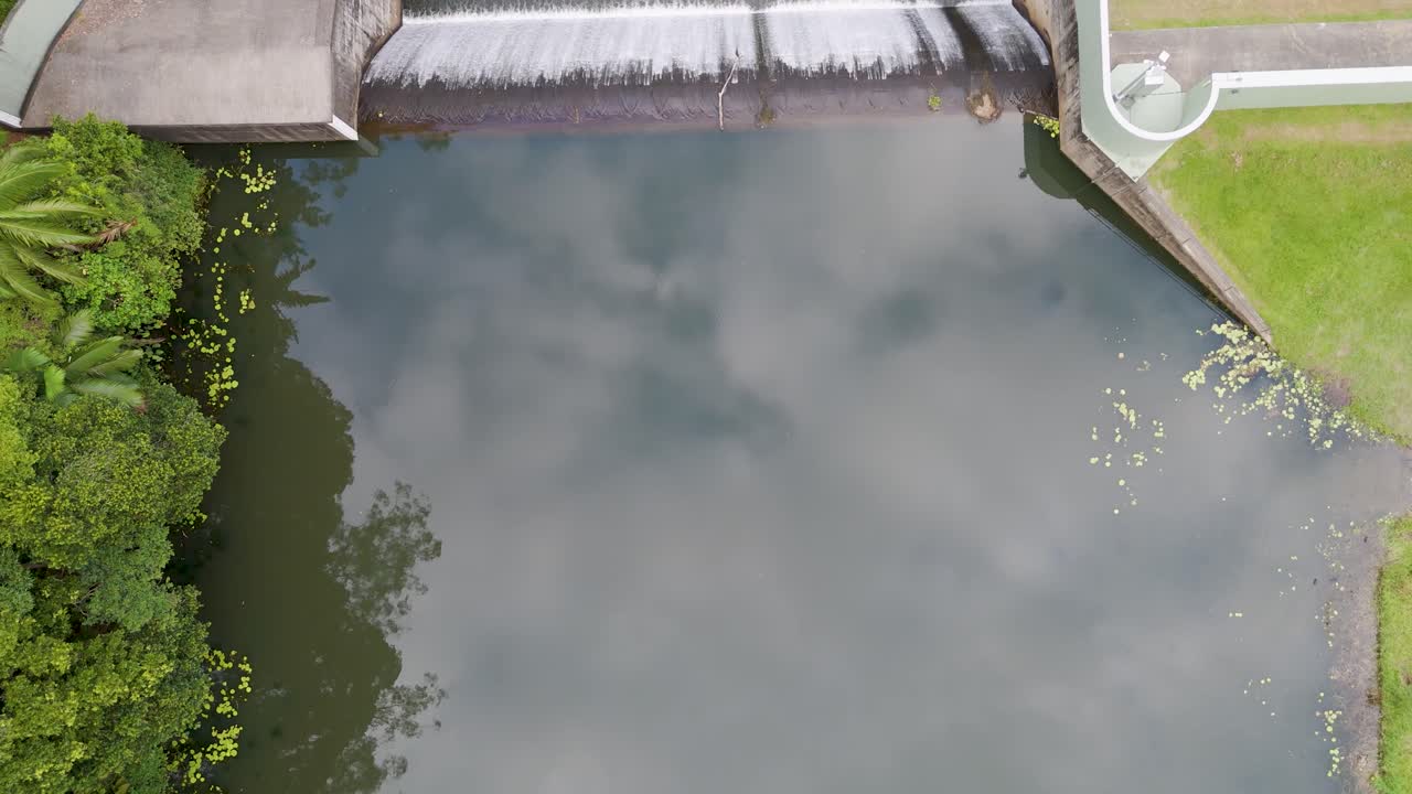 Drone footage captures serene river and dam in Gold Coast, Australia. Lush greenery and calm waters create a tranquil scene