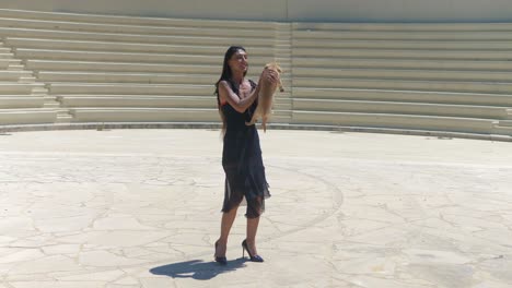 attractive woman in black dress petting her cute kokoni dog pet on amphitheater plateau on sunny day, wide shot