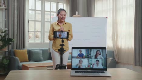 asian female teacher shoots video by smartphone camera and having video call on laptop while teaching english at home