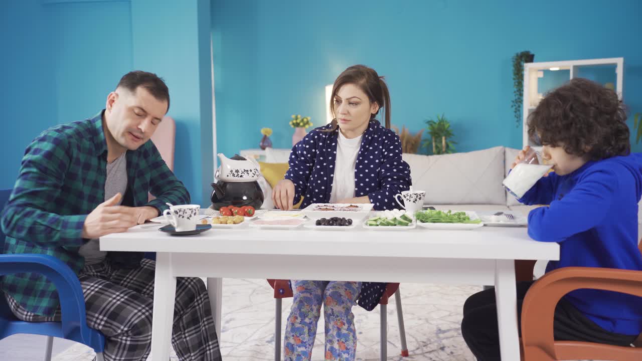 가족들은 집에서 아침 식사를 하고 있으며, 가족의 아버지는 지루하고 일에 압도되어 있습니다.
