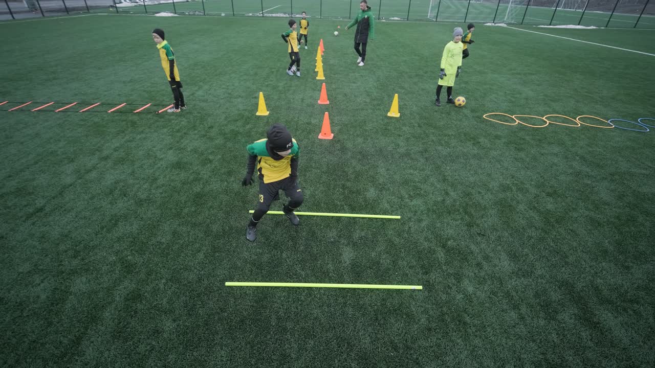 어린이 축구팀은 코치의 지도하에 경기장에서 훈련합니다. 스포츠 유니폼을 입은 아이들은 공 연습을 하고, 기법을 개선하고, 그린 필드에서 팀워크를 개발합니다.