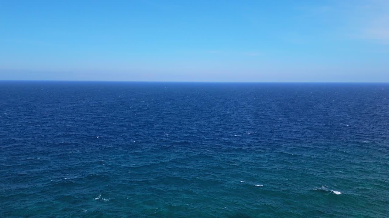 Gentle drone overview of clear open ocean with deep blue mysterious colors reaching to horizon