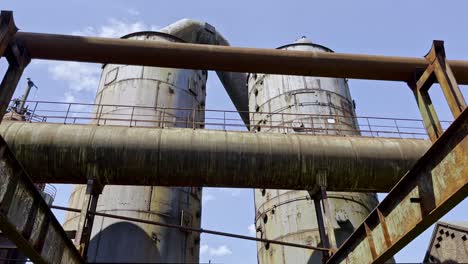 Zwei-Große-Alte-Rostige-Tanks-Mit-Breiten-Metallleitungen-Im-Landschaftspark-In-Duisbrug