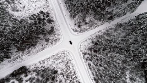 Looking-straight-down-at-a-car-in-the-crossroads-of-a-frozen-winter-landscape-with-a-decision-on-which-direction-to-turn---aerial-spinning-view