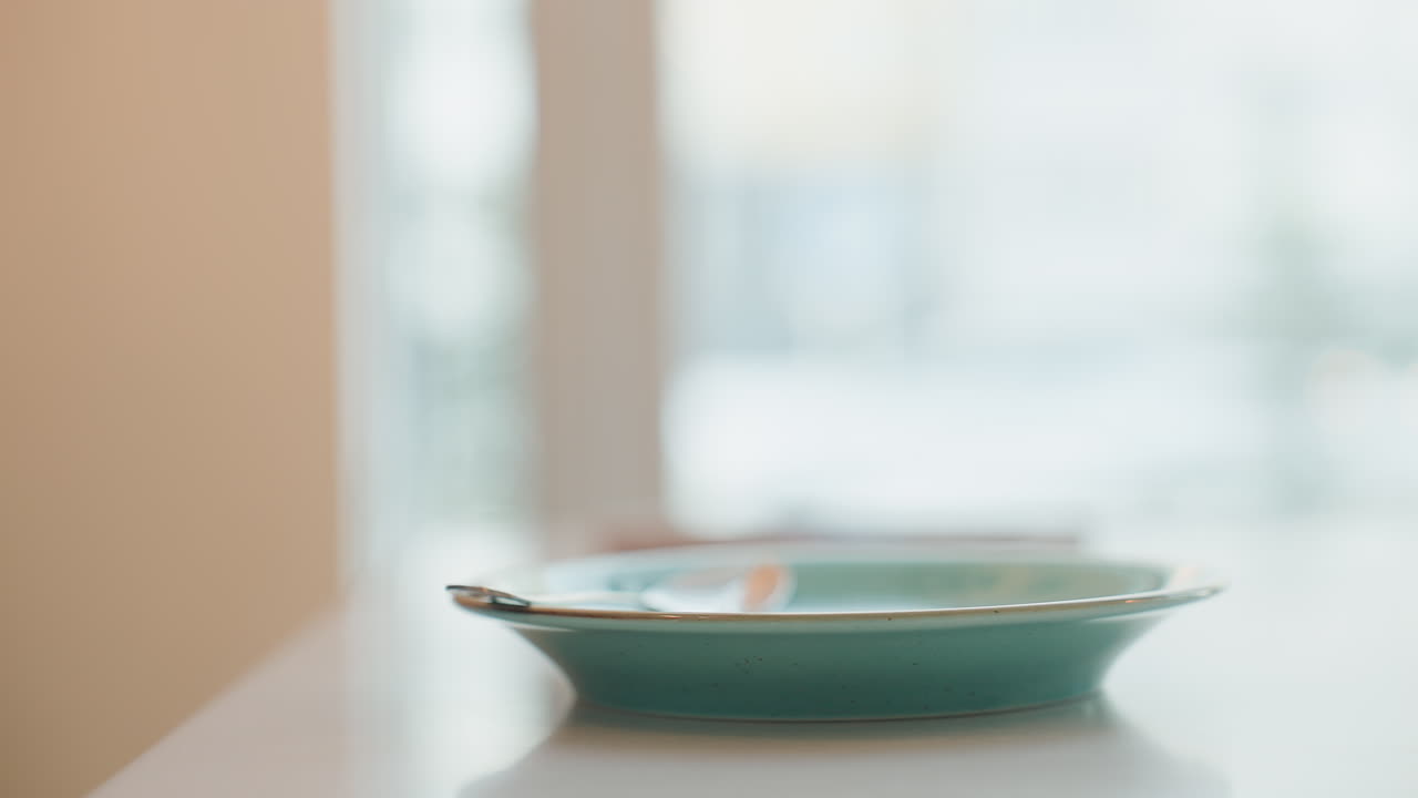 Close-up shot of young woman in cafe gently lifting and sipping beverage, then placing it down on table, through transparent window, cars move on snowy street, creating cozy, calm atmosphere
