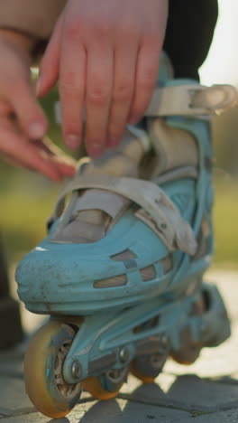 un primer plano de una persona ajustando las correas de una patineta azul claro mientras un pie permanece en una bota negra. el enfoque está en las manos y la patineta, con la otra bota visible