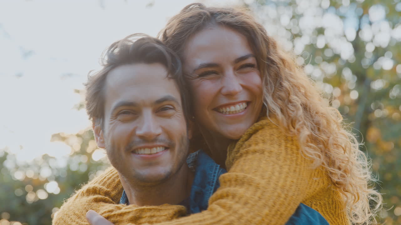 retrato de una pareja feliz y amorosa con un hombre que le da a la mujer un piggyback mientras se abrazan en el parque de otoño juntos