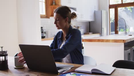 mujer con taza de café usando una computadora portátil en la cocina