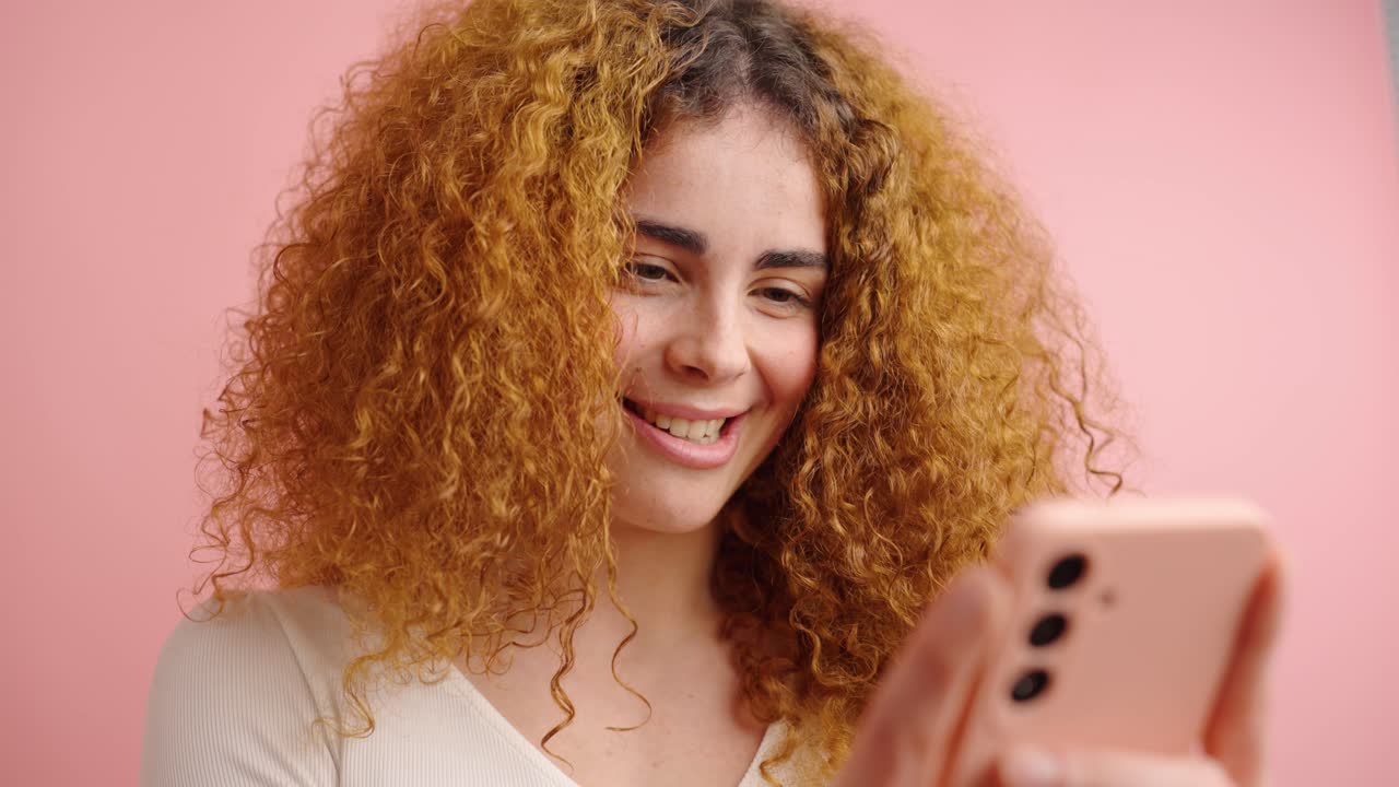 Smiling female using cellphone in pink studio