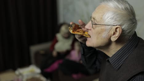 Beautiful-elderly-man-in-glasses-eats-pizza.-His-family-in-background