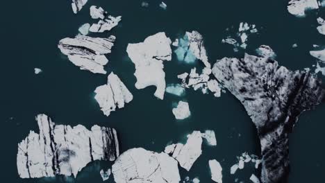 drone shot of beatiful black and white icebergs floating in a dark blue lagoon in iceland