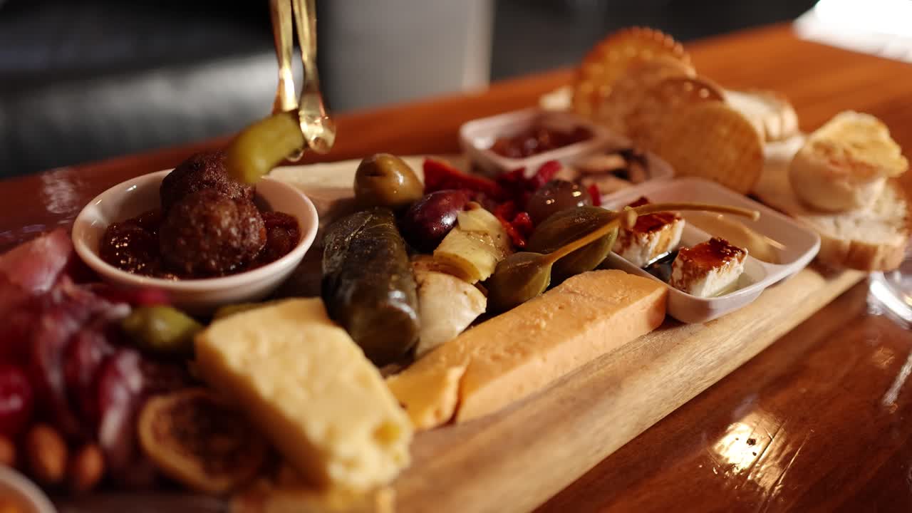 Hand lifts melted cheese from charcuterie board with crackers, pickles, meatballs, and antipasto