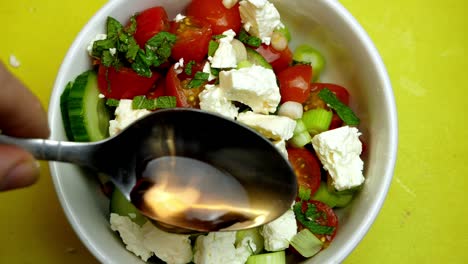 Von-Oben-Nach-Unten-Zeitlupe-Einer-Hand,-Die-Apfelessig-über-Einen-Griechischen-Salat-Mit-Gelbem-Hintergrund-Gießt