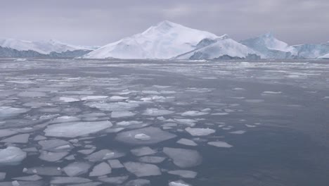 slow motion video of a large iceberg and smaller ice floes in the foreground off the coast of greenland