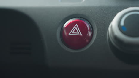 close up of individual pressing red hazard warning button on car dashboard interior showing finger interaction with emergency control switch near climate dial in modern vehicle cabin