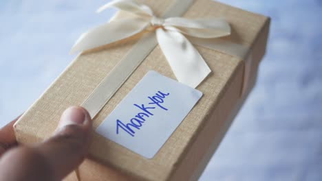 hand holding a light brown gift box with a thank you tag