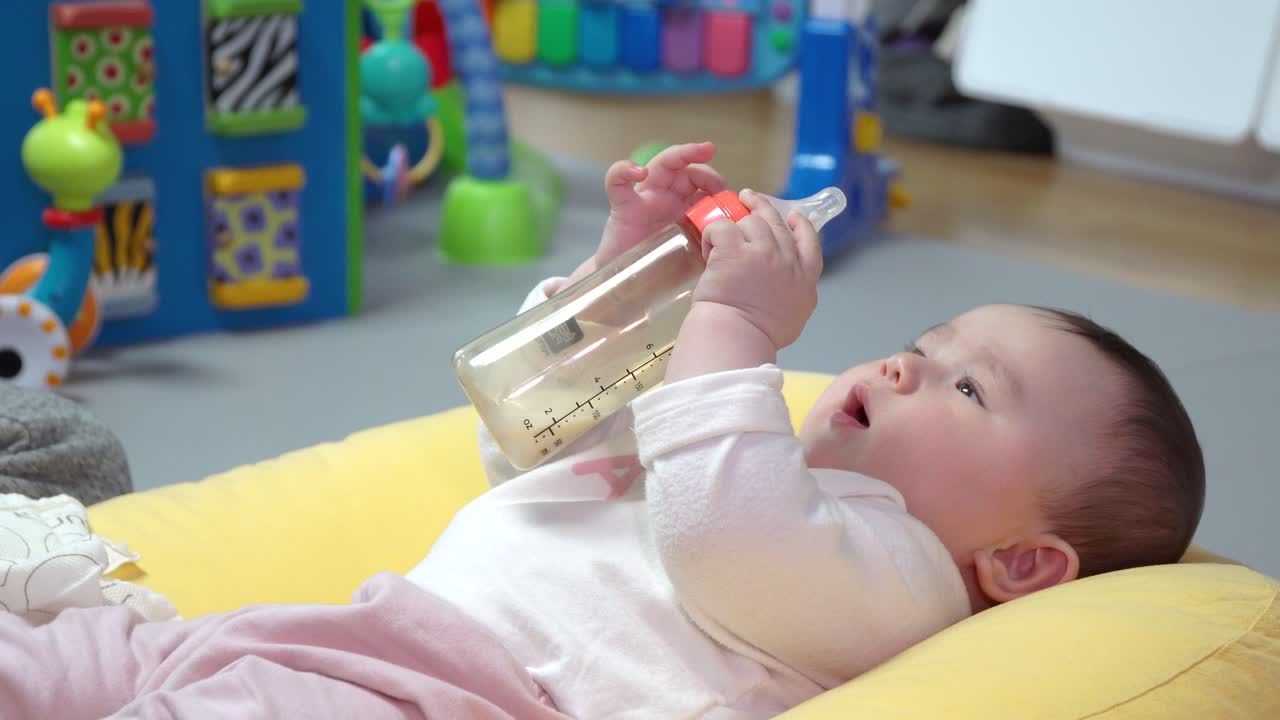 그녀의 먹이 병을 재생 쿠션에 다시 누워 건강한 여자 아기