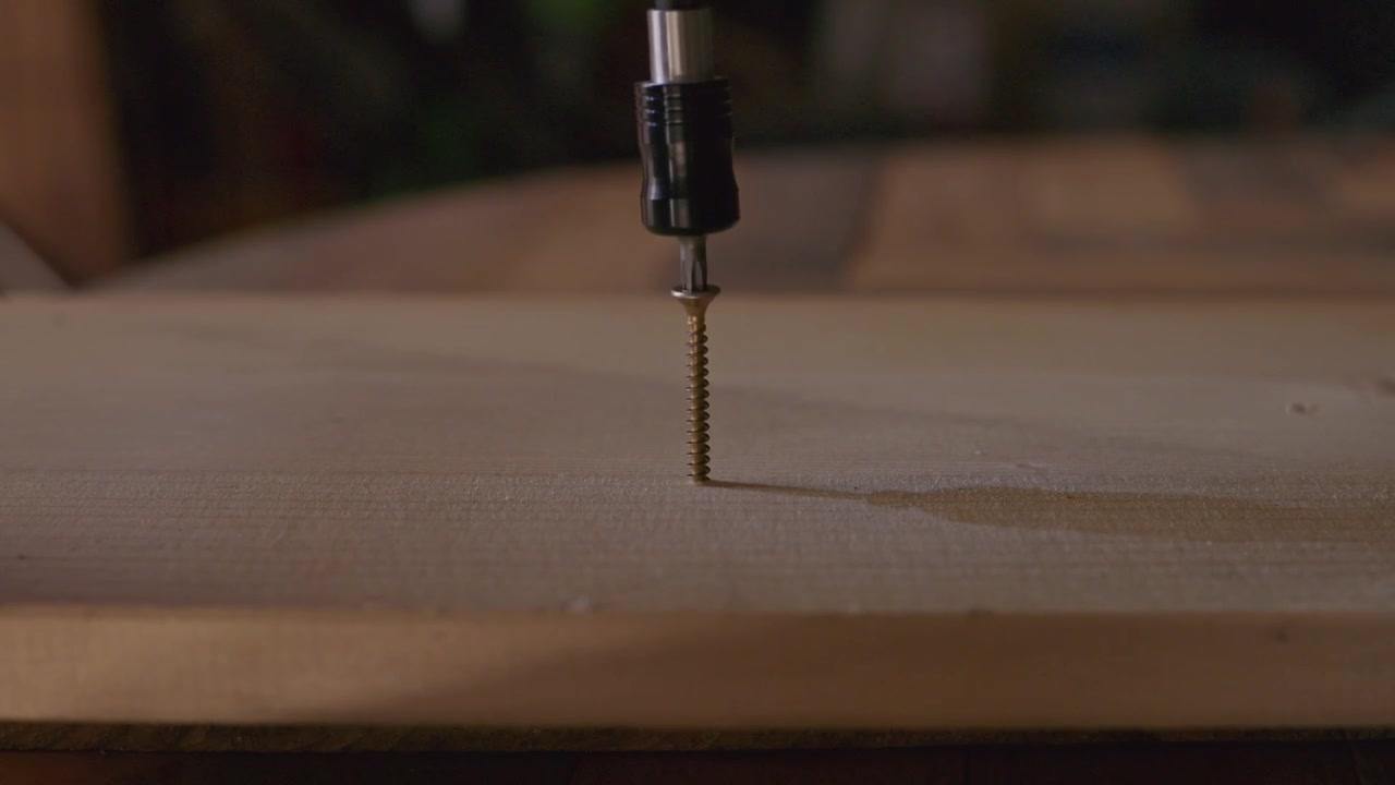 Primo piano di un avvitatore elettrico che inserisce una vite di metallo nel legno, rappresentando edilizia, falegnameria, montaggio di mobili, riparazioni e lavori fai-da-te