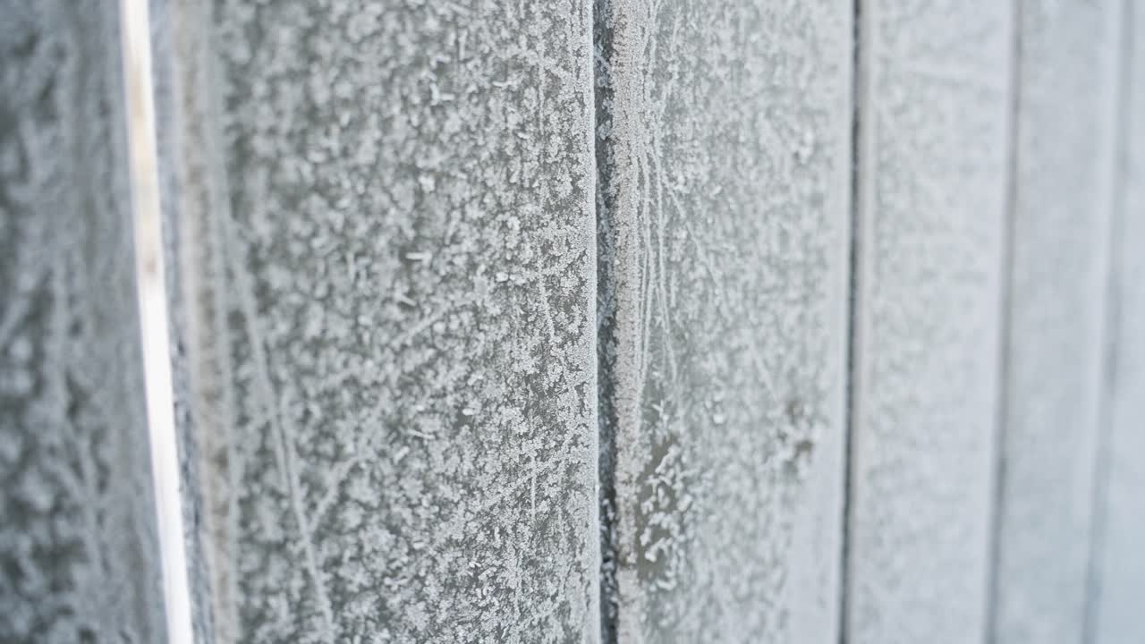 Nærbilde av et tregjerde dekket med frost, som viser isete tekstur og vintermønstre på vertikale planker i kaldt morgenlys, ideelt som sesongbasert bakgrunn b-roll